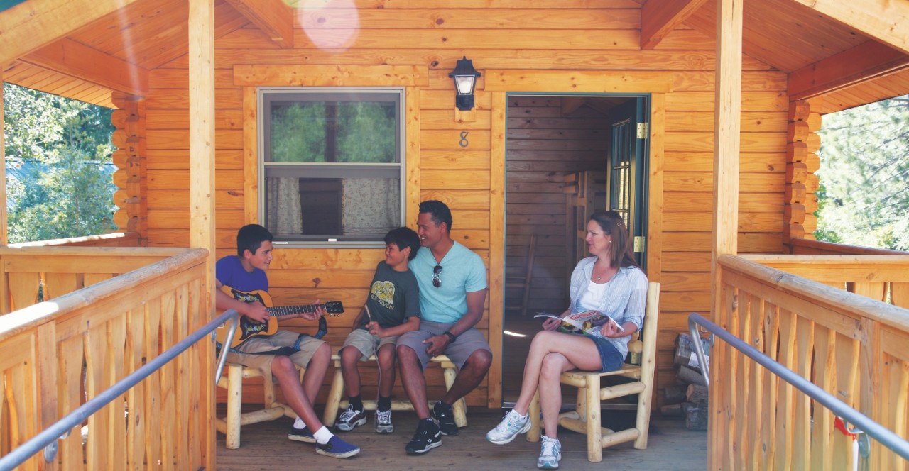 A family of four happily sitting in front of a camp cabin